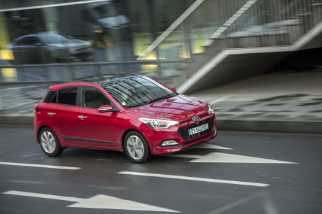 Hyundai i20 2016 creative rouge roulant en ville devant une vitrine