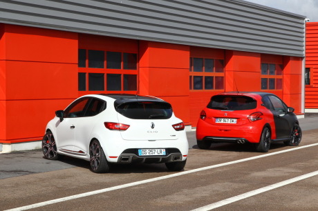 208 GTi by Peugeot Sport vs Renault Clio RS 220 EDC Trophy garées cote a cote devant un batiment rouge vue arriere